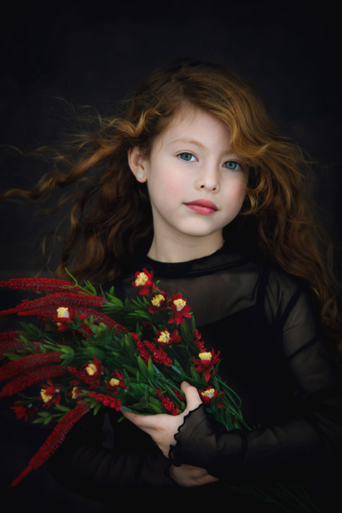 stunning girl classic portrait. She is a beautiful girl with green eyes and red hair, holding a bouquet of red flowers a very elegant portrait of a young lady